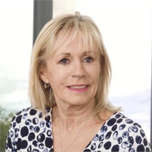 Linda Woolterton in a white top with black dots, in front of a window