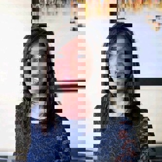 Tejal Shah in a blue lacey top in front of a plain wall with a painting hanging on it.