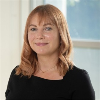 Tanya Jones wearing a black top in front of a blurry background.