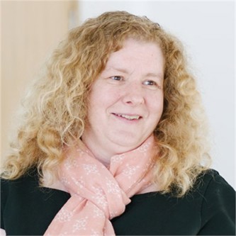 Zoe Cooke wearing a light pink scarf, black top and brown and grey background.