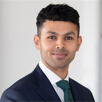Shy Islam in a dark jacket and green tie, in front of a pale background