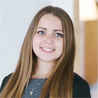 Louise Riseborough in a black jacket and patterned top, in front of a pale background