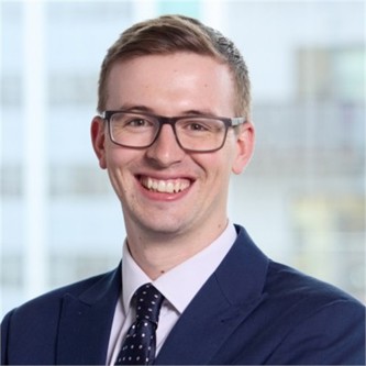 Ed Wrightson in glasses, and a blue suit and tie, in front of a window