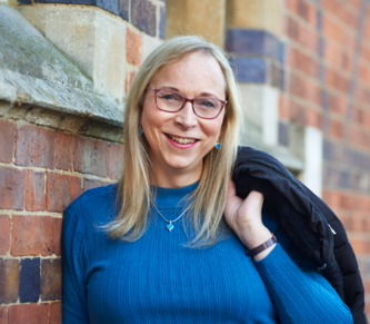 Katie Neeves in a blue jumper standing in front of a brick wall.