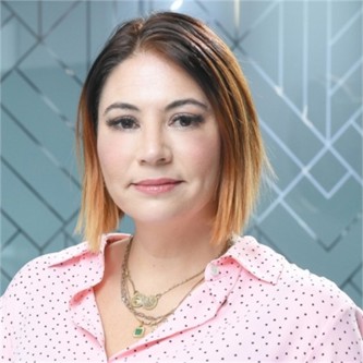 Miranda Perks in a pale pink spotty top, in front of a geometric glass background