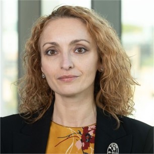 Aneta Lorens-Boursier in a black jacket and yellow top, in front of a window