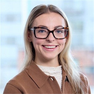 Freya Mayall in glasses and a brown jacket, in front of a window