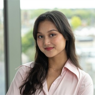 Valentine Doan wearing a pink formal shirt in front of a blurry background.