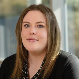 Sophie Ball in a black cardigan and spotty shirt, in front of a window