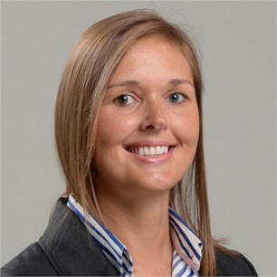 Elaine Mitchell in a dark jacket and striped shirt, in front of a grey background