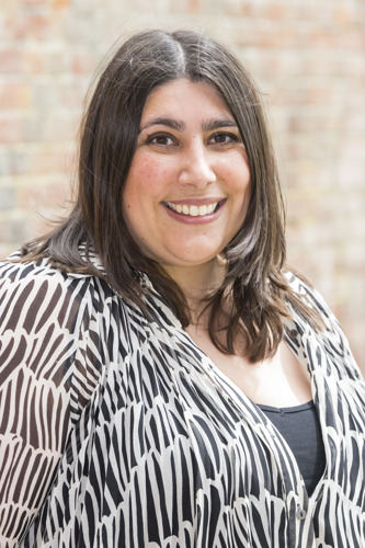 Louise Birritteri in a black and white patterned top in front of a brick wall.