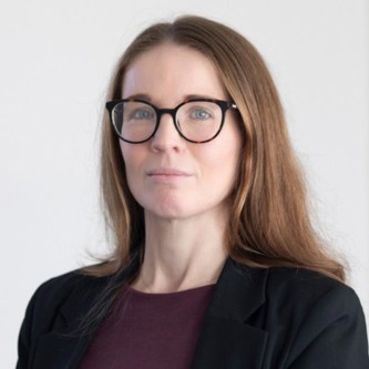 Madeline Turner wearing glasses, burgundy top, black blazer with a light grey background.