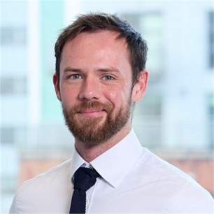 Will Marlow wearing a navy blue tie, white formal shirt in front of a blurry building.
