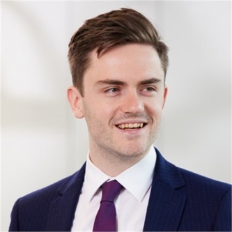 Robert Jackson in a navy jacket and purple tie, in front of a pale background