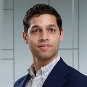 Ashish Patel in a blue jacket, in front of a geometric glass background