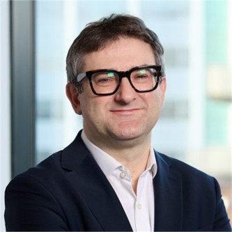 Ian Hardman in glasses, a dark jacket and white shirt, in front of a window