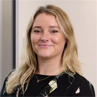 Abbie Green in a black patterned jacket, in front of a grey background
