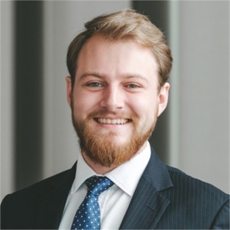 James Dorrell in a dark pinstripe suit, and blue tie, in front of a grey background