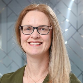 Jennie Newton in glasses and a green jacket, in front of a geometric glass background