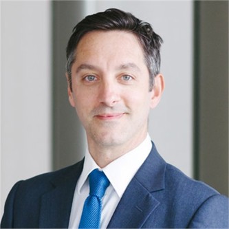 Vincenzo Maggio wearing a blue tie, white formal shirt, blue blazer in front of a grey background.