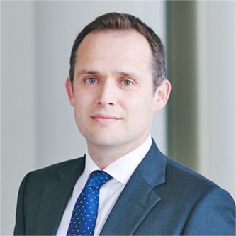 Douglas McDonald in a blue suit and tie, in front of a grey background