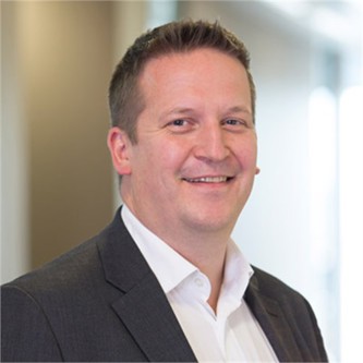 Niall Innes in a dark jacket and white shirt, in front of a window