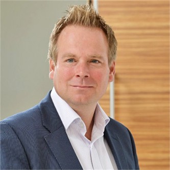 Richard Santy in a blue jacket and white shirt, in front of a door