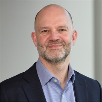 Chris Belcher in a dark suit, in front of a grey background