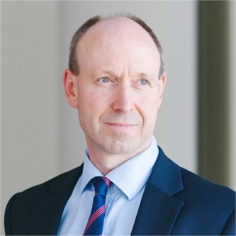 Michael Aubrey in a blue shirt and tie, in front of a grey background