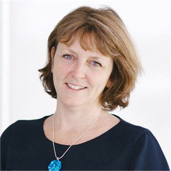 Sarah Seed in a dark top and statement necklace, in front of a pale background