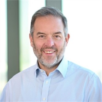 Neil Burton in a pale blue shirt, in front of a window