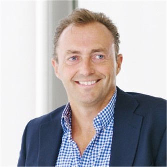 David Mills in a navy jacket and check shirt, in front of a pale background