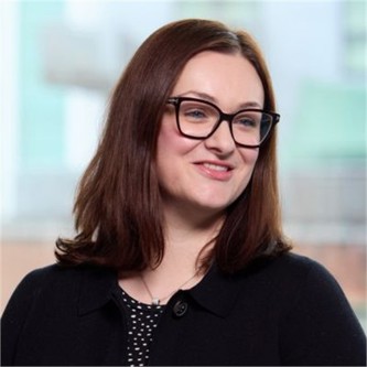 Melanie Grimshaw in glasses, a black jacket and black spotty top, in front of a window
