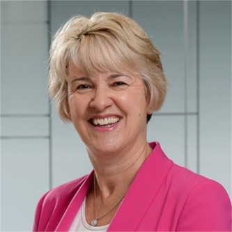 Jill Mason in a pink jacket, in front of a geometric glass background